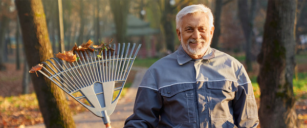 Rentner in Arbeitskleidung mit Rechen bei der Grünanlagenpflege