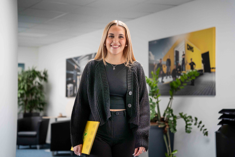 Junge Mitarbeiterin mit Unterlagen in einem modernen Büroflur.