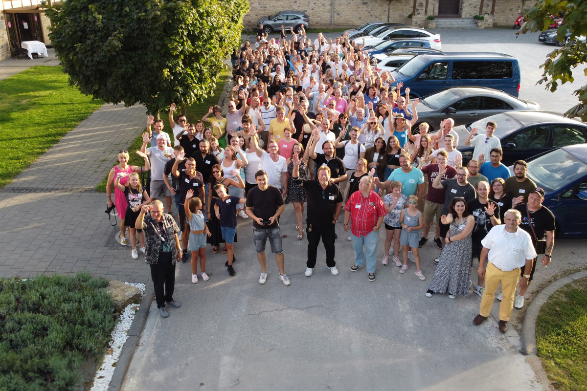 Große Gruppe von Mitarbeitenden und Familien beim Sommerfest, aufgenommen aus der Vogelperspektive auf einem Hofgelände.