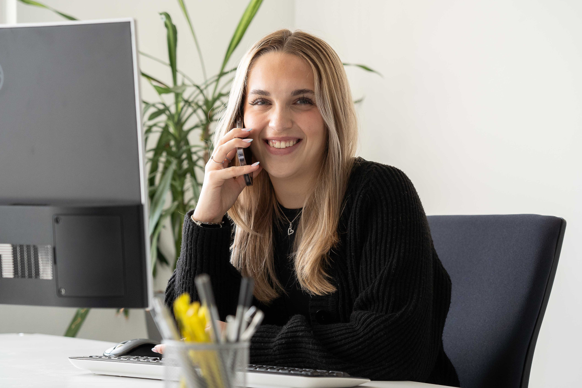 Mitarbeiterin telefoniert am Schreibtisch und arbeitet an einem Computer in einem modernen Büro.