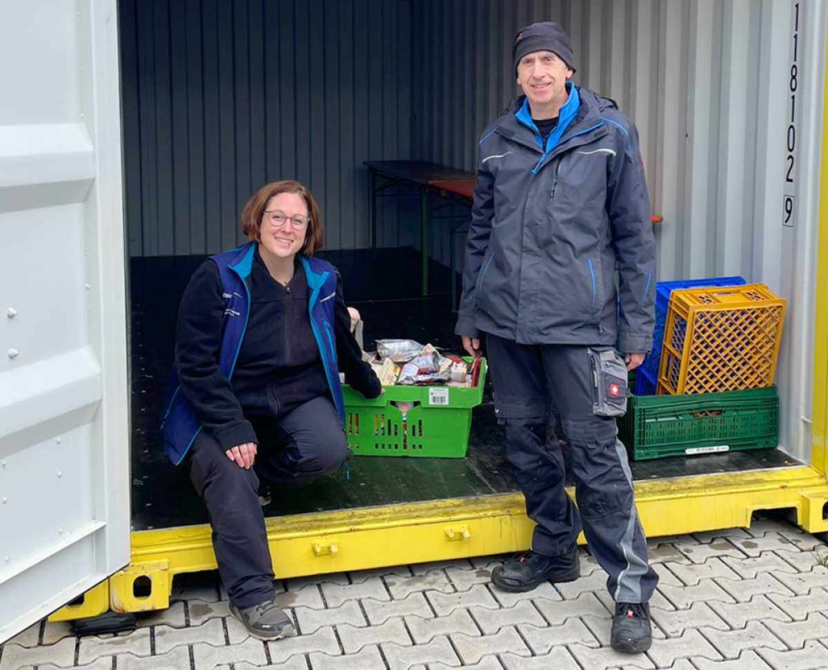 Zwei Mitarbeitende sortieren Futter‑ und Sachspenden in einem geöffneten Container