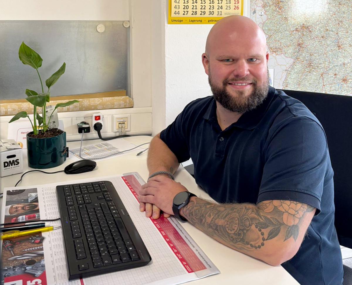 Mitarbeiter sitzt am Schreibtisch im Büro vor Tastatur und Unterlagen.