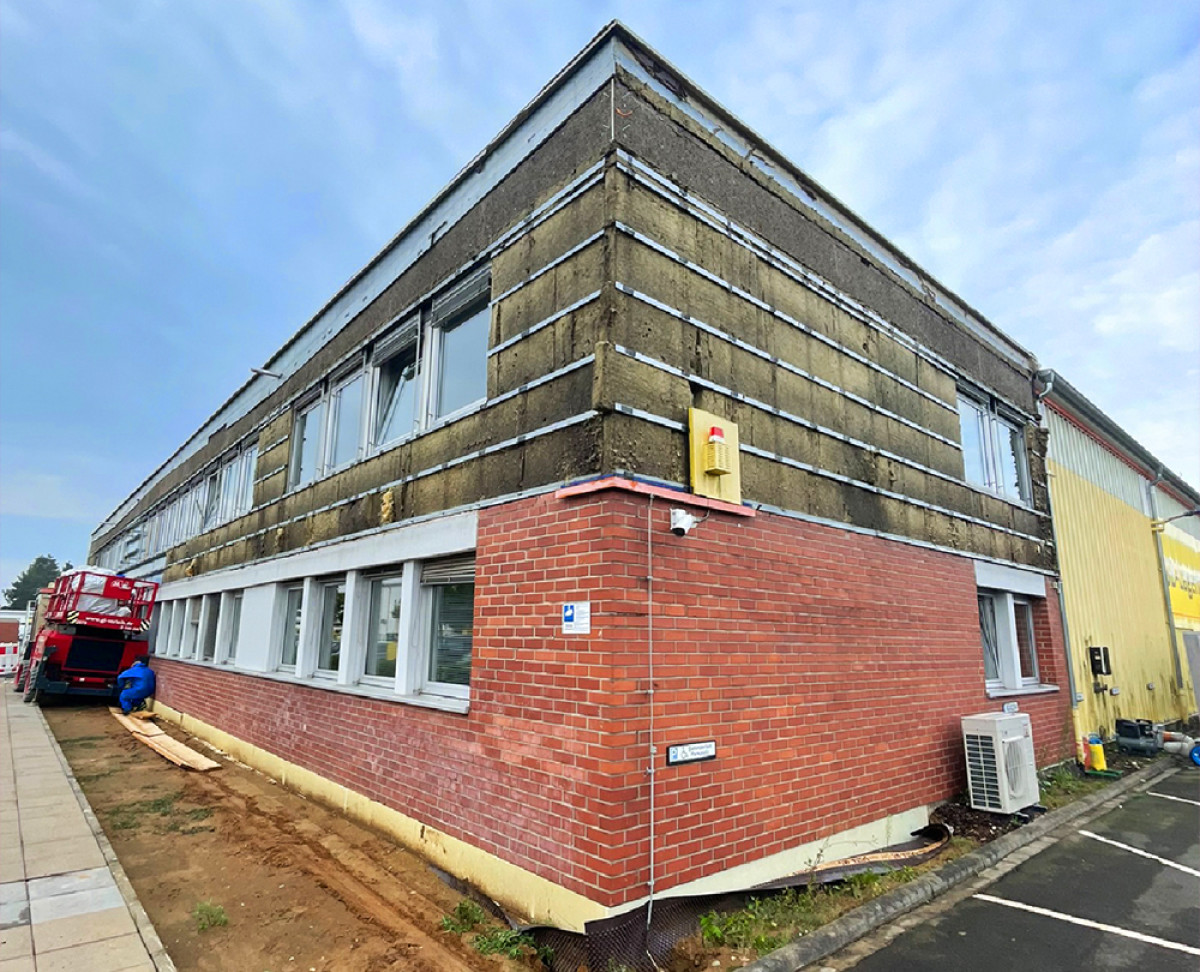 Gebäude während der Fassadensanierung mit sichtbarer Dämmung und Baugeräten.