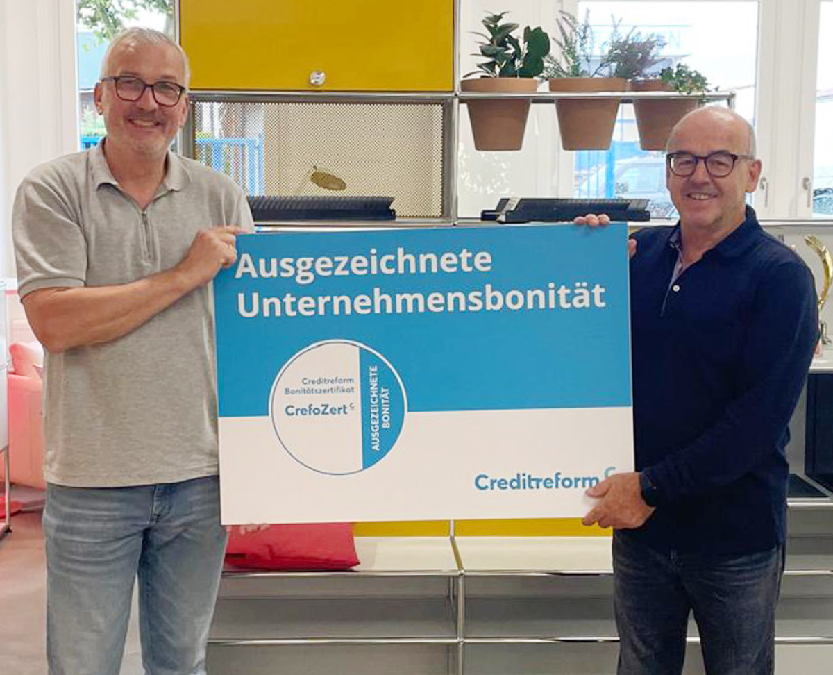 Mitarbeitende halten ein CrefoZert-Schild für ausgezeichnete Unternehmensbonität von Creditreform.