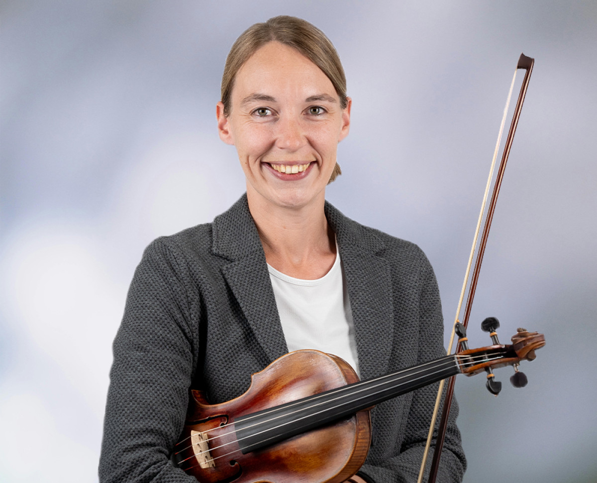 Person in Businesskleidung hält eine Violine und einen Bogen vor neutralem Hintergrund.