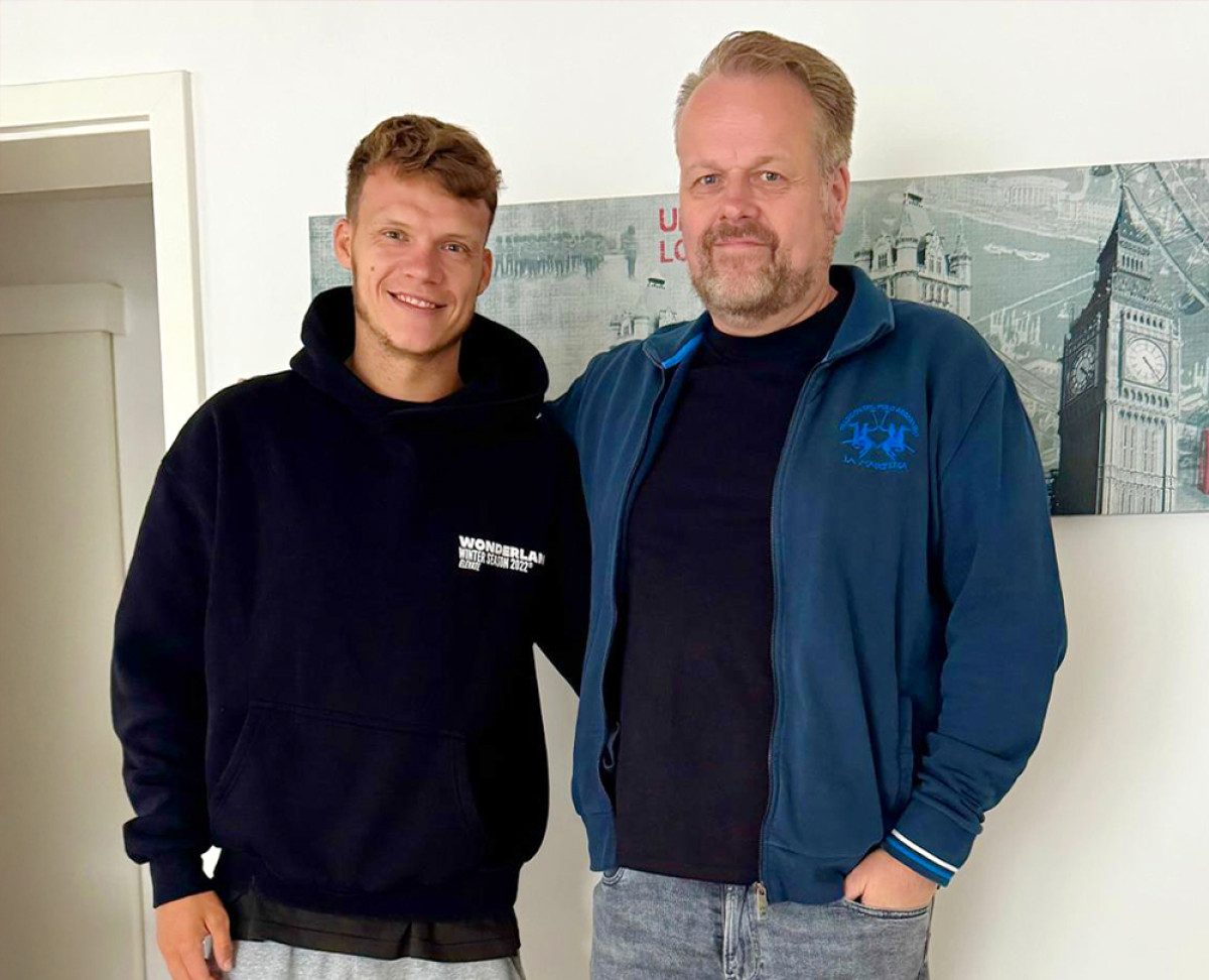 Zwei Personen stehen nebeneinander in einem Innenraum vor einem Wandbild mit London‑Motiven.