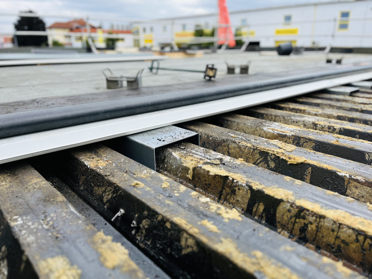 Detailaufnahme eines Metallgitters auf einer Baustelle mit aufliegendem Profil und sichtbaren Befestigungselementen.“