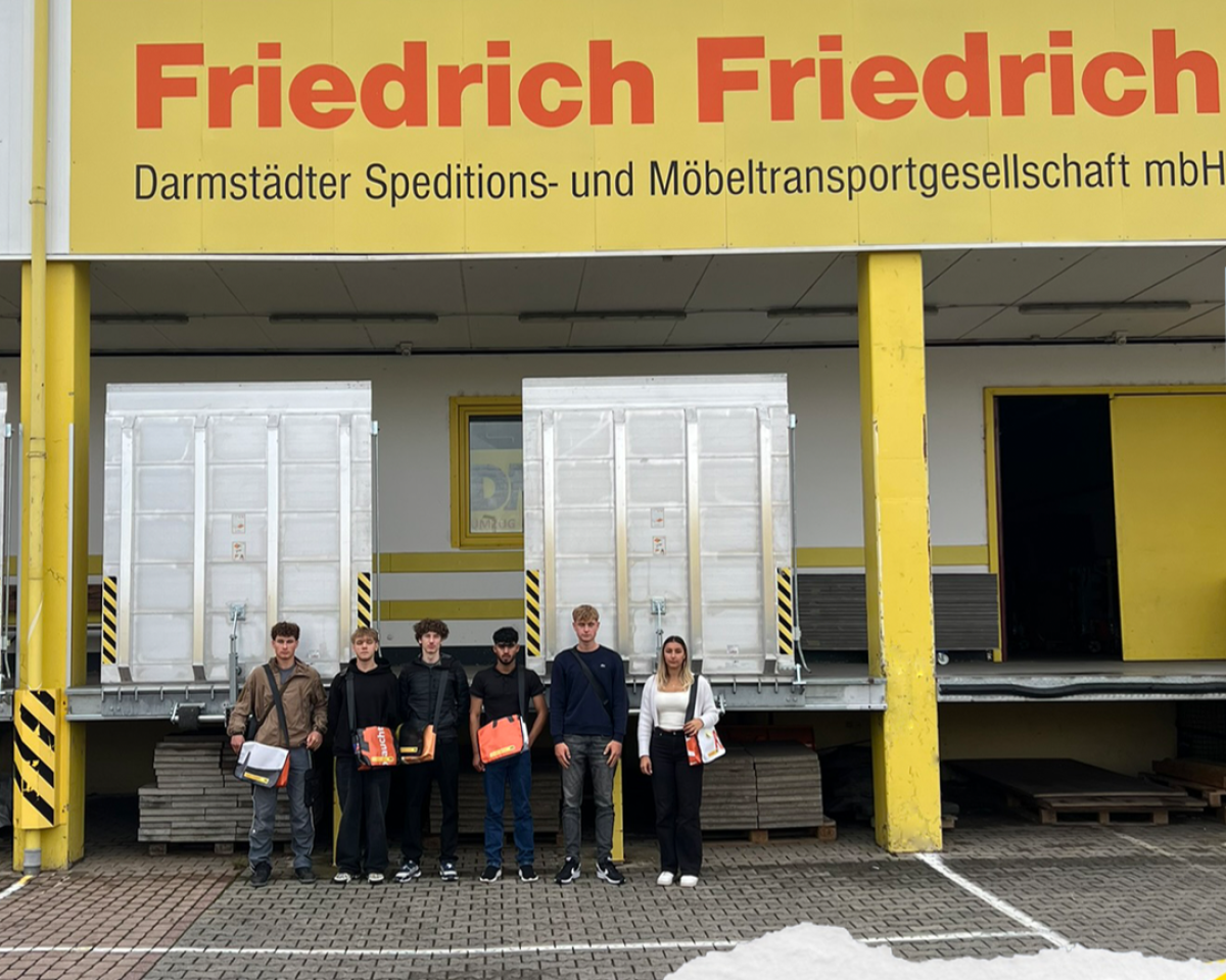 Gruppe von Auszubildenden steht vor dem Firmengebäude von Friedrich Friedrich, einer Speditions‑ und Möbeltransportgesellschaft.
