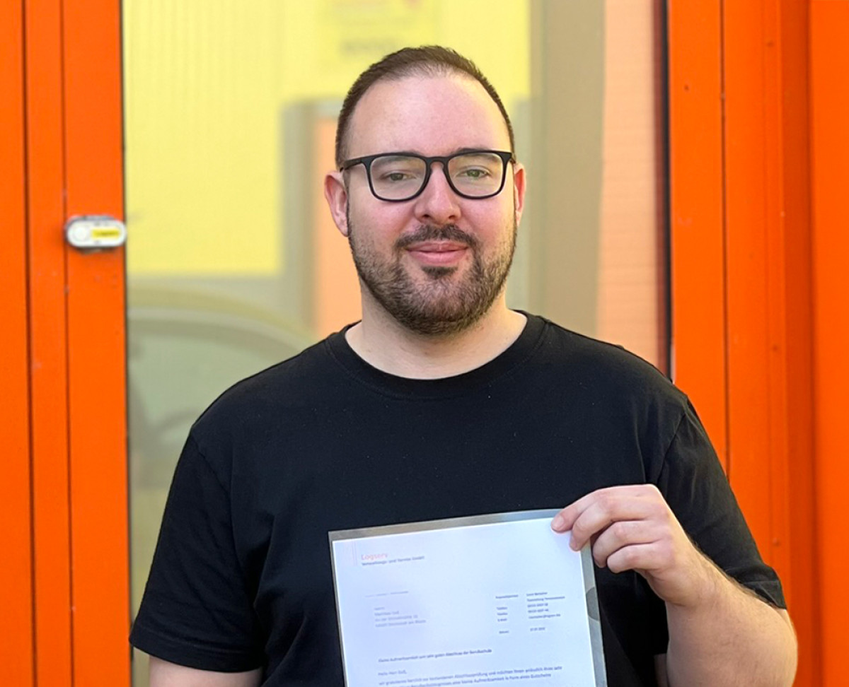 Person hält ein Dokument vor einem orangefarbenen Eingangsbereich des Unternehmens.