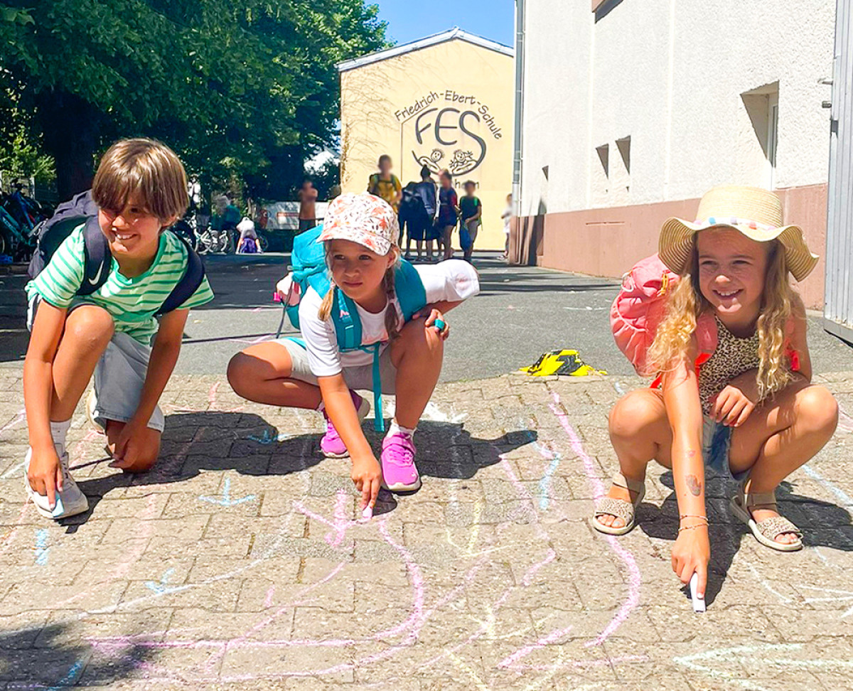 Kinder malen mit bunter Kreide auf dem Schulhof der Friedrich‑Ebert‑Schule.