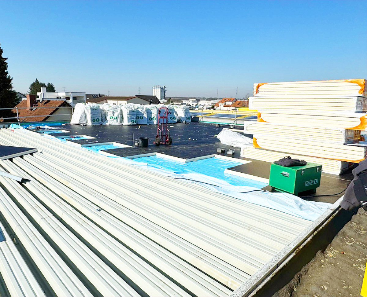 Dachsanierung mit Dämmmaterial und Bauelementen auf einem Flachdach bei sonnigem Wetter.