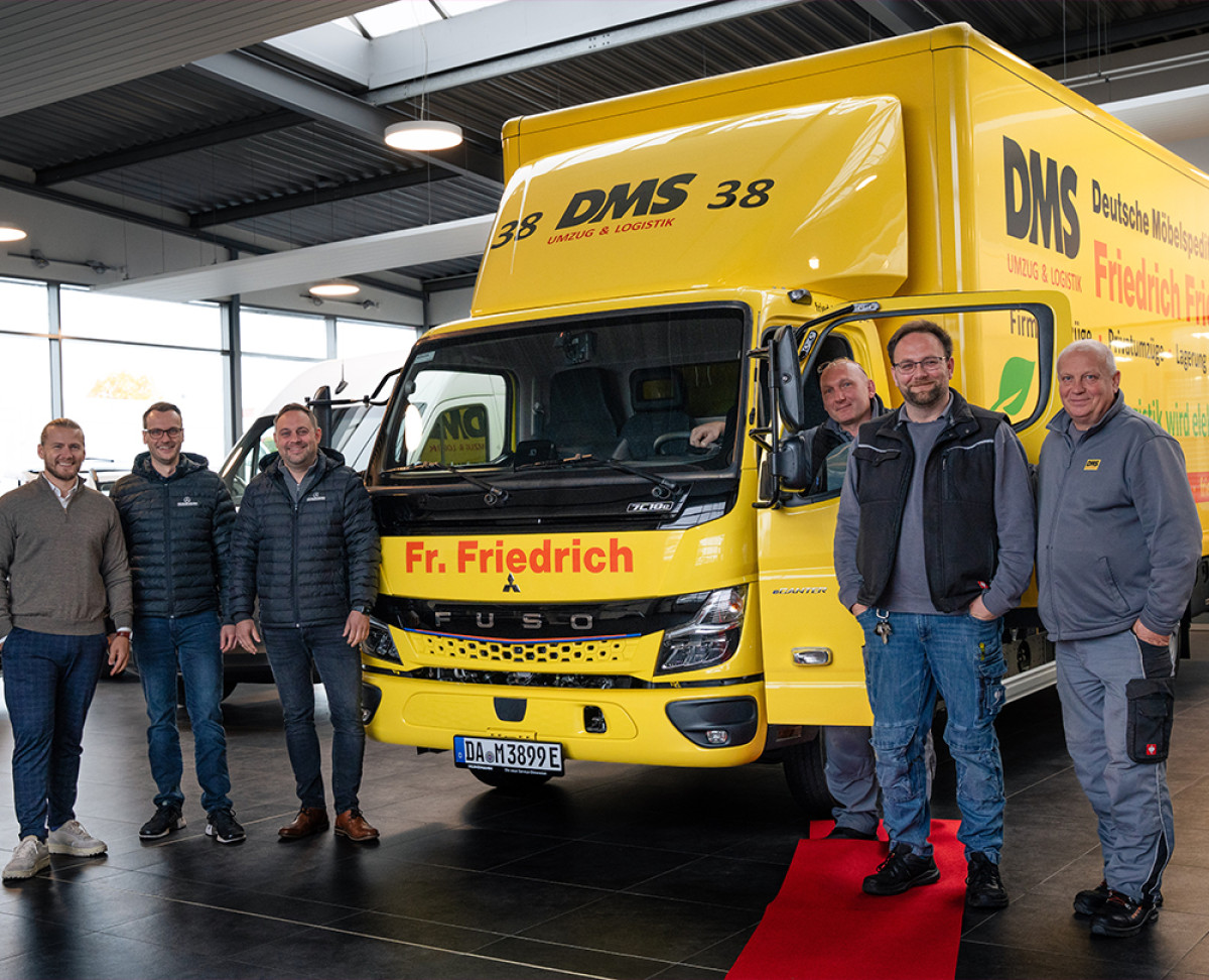 Übergabe eines neuen gelben DMS‑Lkw von Friedrich Friedrich an das Team in einer Fahrzeughalle