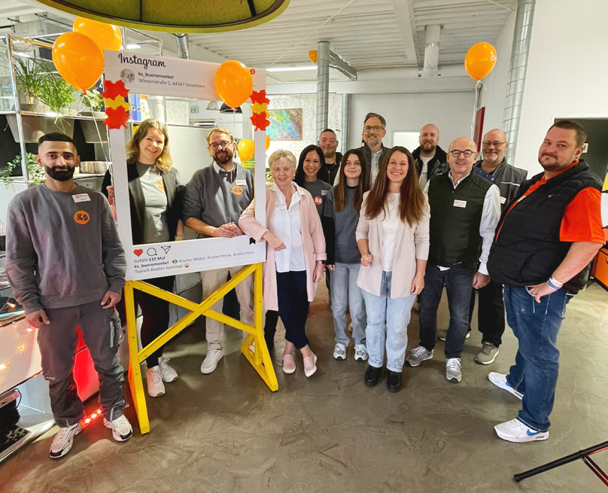 Gruppenfoto beim KS‑Knaller‑Samstag mit Mitarbeitenden und Azubis vor einem dekorierten Instagram‑Rahmen und Luftballons