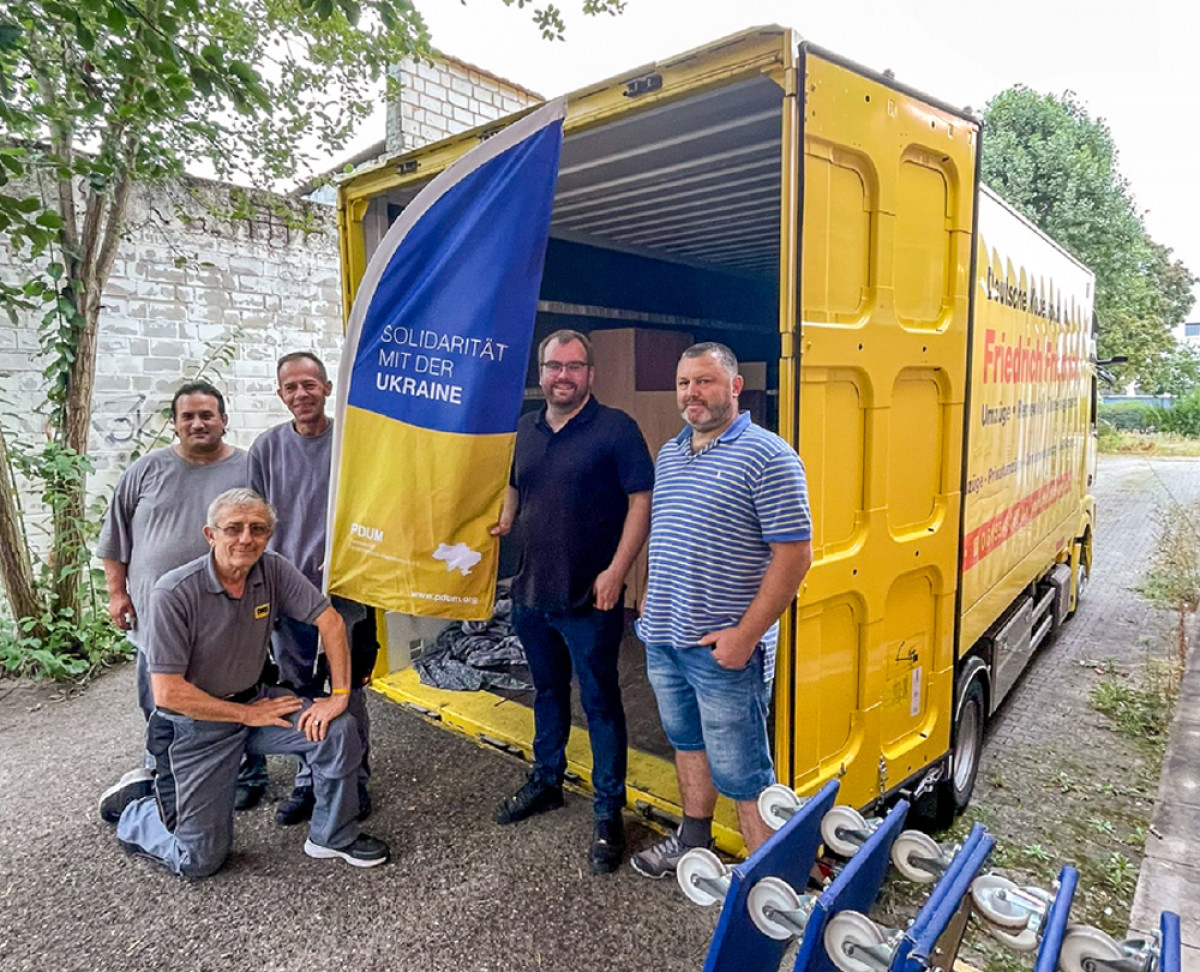 Team vor einem geöffneten Umzugsfahrzeug mit Fahne zur Solidarität mit der Ukraine.