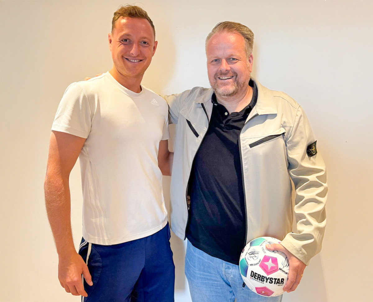 Zwei Personen stehen nebeneinander, eine hält einen Derbystar‑Fußball, vor hellem Hintergrund.