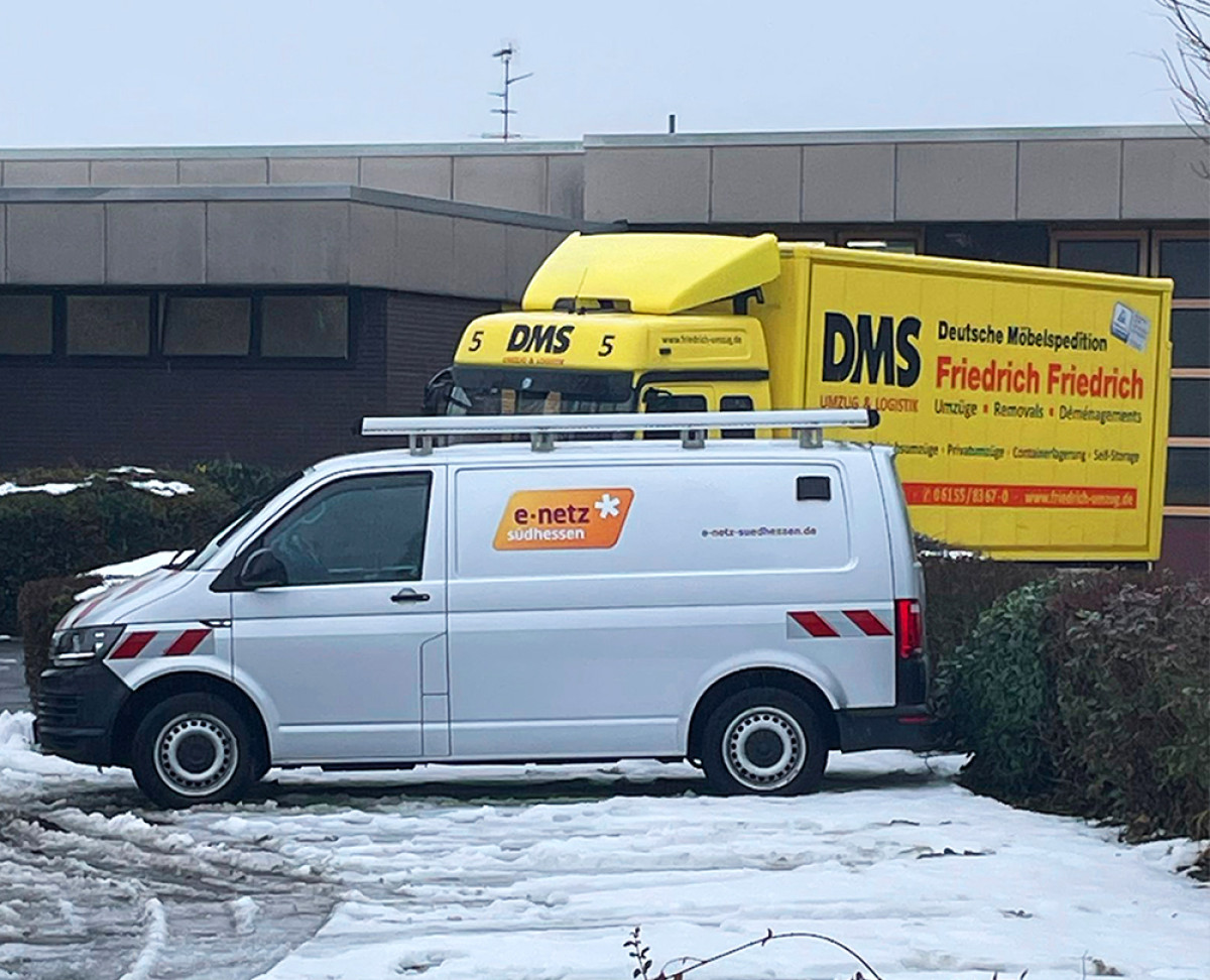 Servicefahrzeug von e‑netz Südhessen und gelber DMS‑Umzugslastwagen stehen im verschneiten Außenbereich eines Firmengebäudes.
