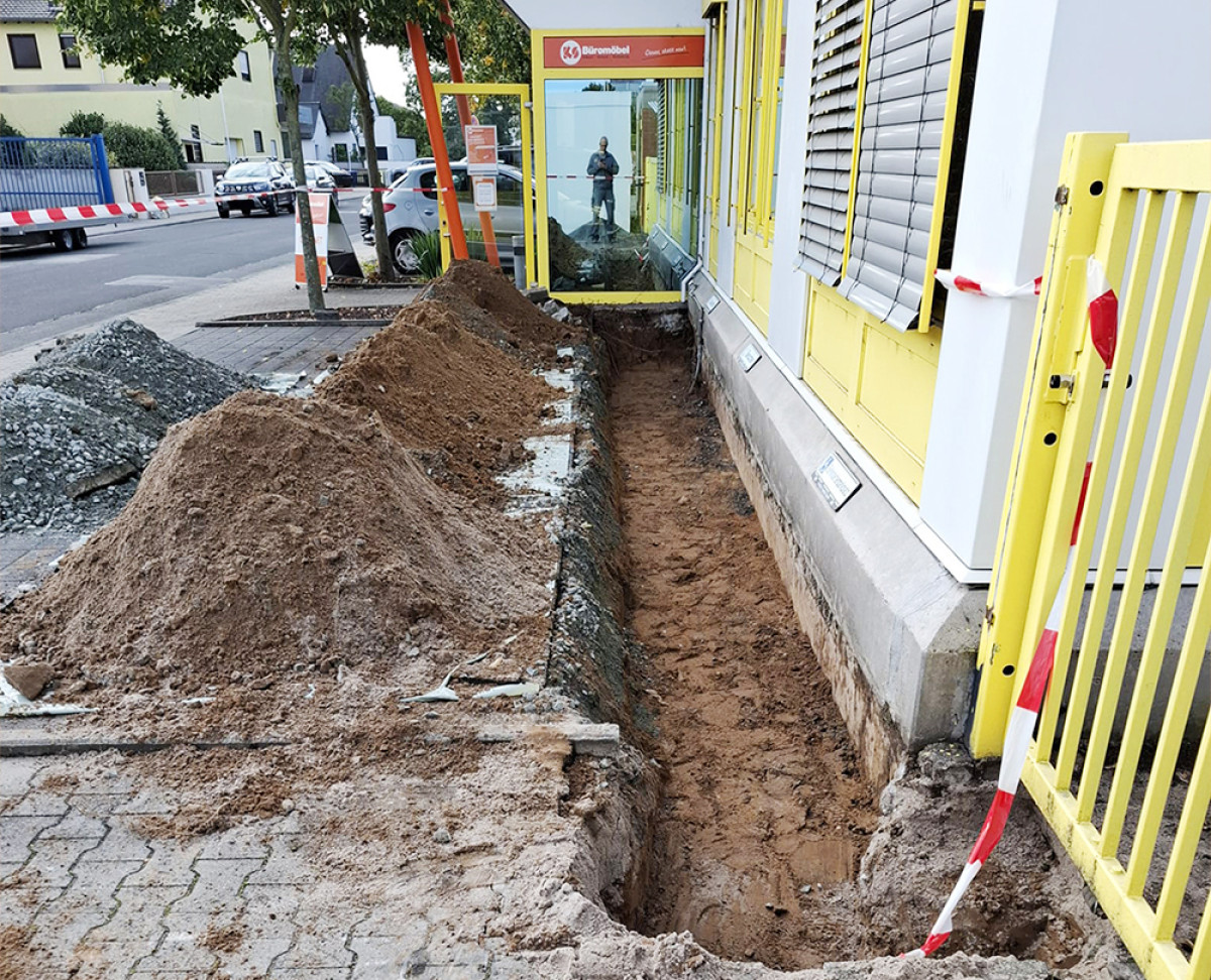 Baustelle vor dem Eingang von KS Büromöbel mit ausgehobenem Graben und Erdhaufen entlang der Fassade.