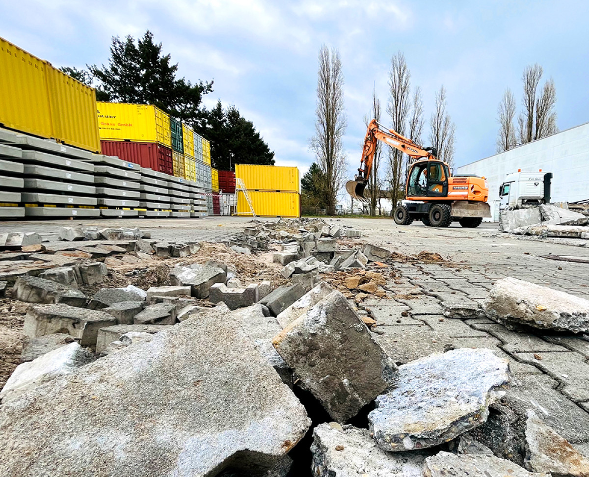 Bagger reißt beschädigte Pflastersteine bei Flächensanierung auf Industriegelände auf