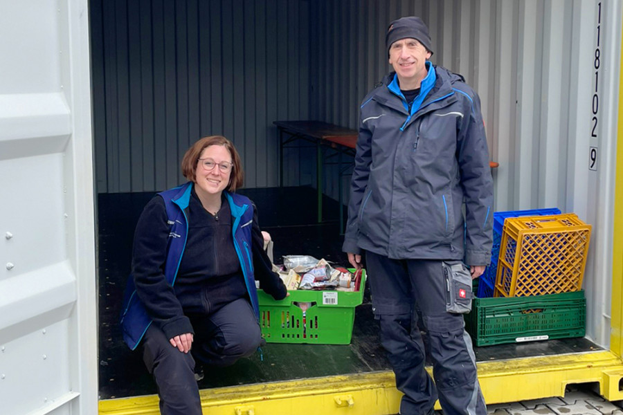 Zwei Mitarbeitende sortieren Futter‑ und Sachspenden in einem geöffneten Container