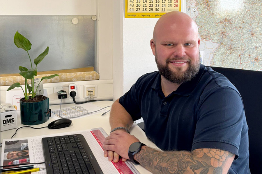Mitarbeiter sitzt am Schreibtisch im Büro vor Tastatur und Unterlagen.