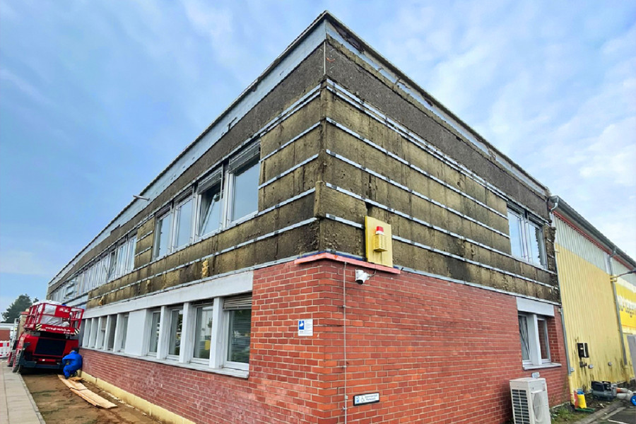 Gebäude während der Fassadensanierung mit sichtbarer Dämmung und Baugeräten.