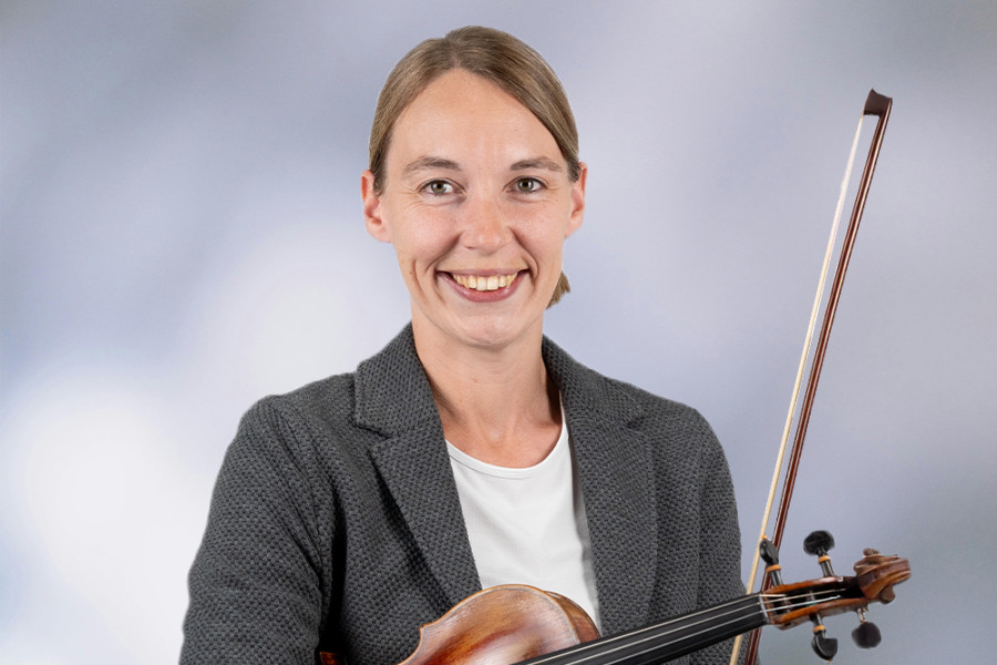 Person in Businesskleidung hält eine Violine und einen Bogen vor neutralem Hintergrund.