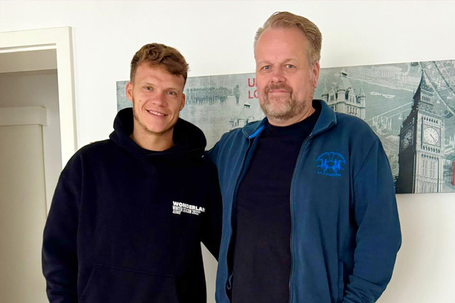 Zwei Personen stehen nebeneinander in einem Innenraum vor einem Wandbild mit London‑Motiven.