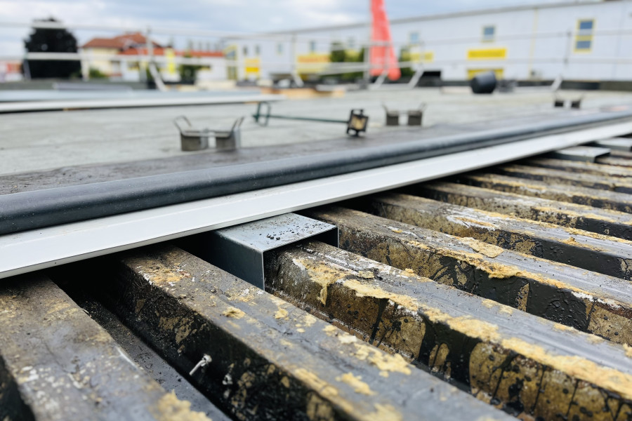 Detailaufnahme eines Metallgitters auf einer Baustelle mit aufliegendem Profil und sichtbaren Befestigungselementen.“