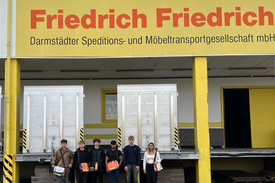 Gruppe von Auszubildenden steht vor dem Firmengebäude von Friedrich Friedrich, einer Speditions‑ und Möbeltransportgesellschaft.