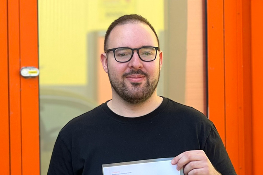 Person hält ein Dokument vor einem orangefarbenen Eingangsbereich des Unternehmens.