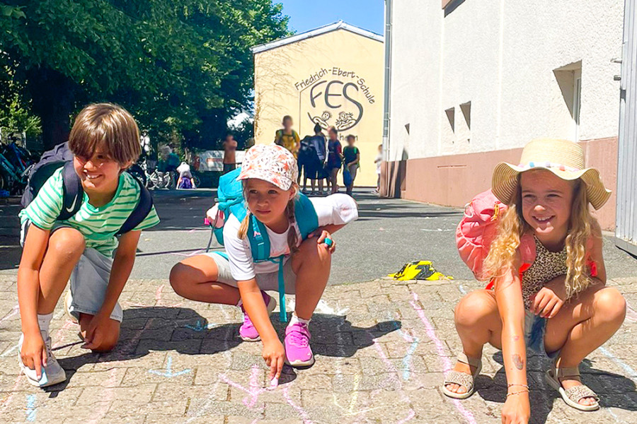 Kinder malen mit bunter Kreide auf dem Schulhof der Friedrich‑Ebert‑Schule.