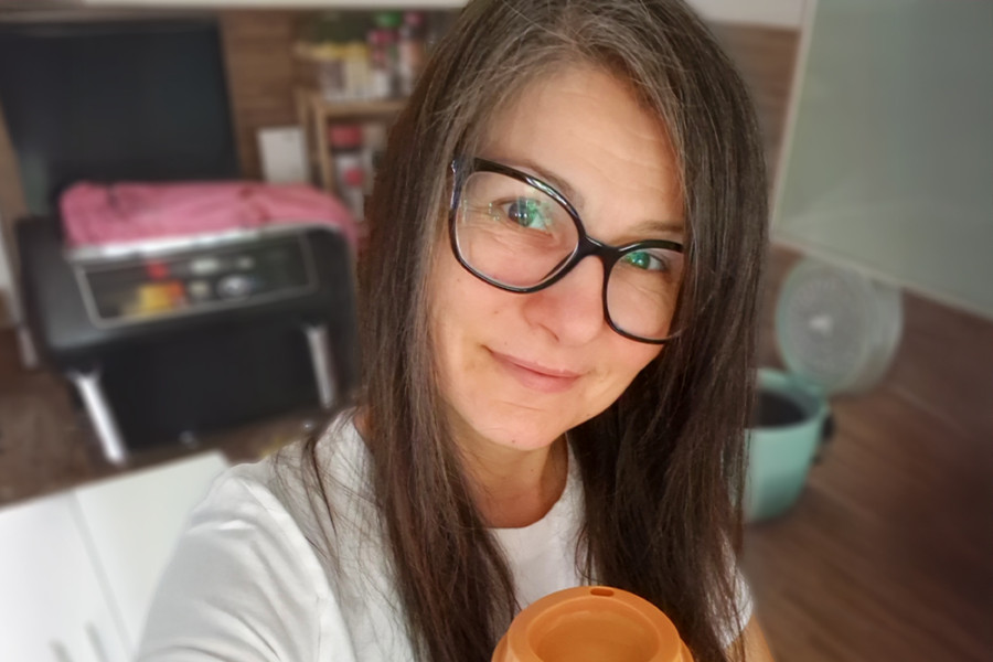 Person hält einen farbigen Mehrwegbecher in der Küche eines Büros oder Wohnbereichs.