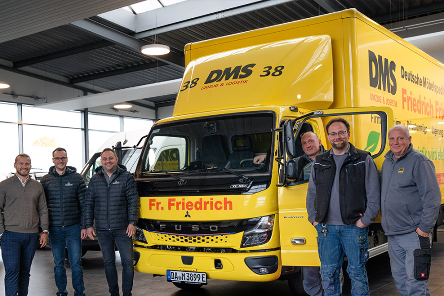 Übergabe eines neuen gelben DMS‑Lkw von Friedrich Friedrich an das Team in einer Fahrzeughalle