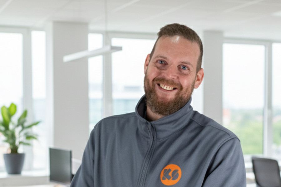 Mitarbeiter in KS‑Arbeitsjacke steht in einem modernen Büro mit großen Fenstern