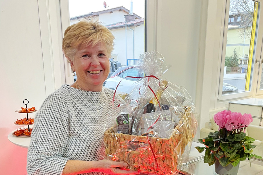 Mitarbeiterin hält einen Geschenkekorb bei einer Abschiedsfeier in einem hellen Büroraum