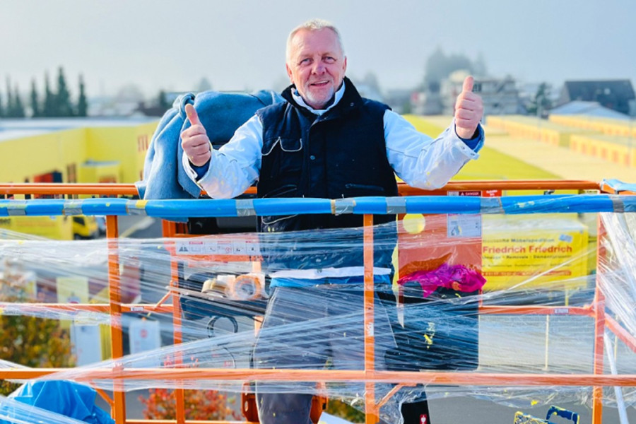 Mitarbeiter zeigt Daumen hoch auf einer Arbeitsbühne vor dem Gelände von Friedrich Friedrich