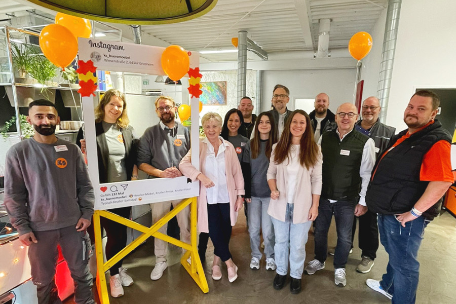 Gruppenfoto beim KS‑Knaller‑Samstag mit Mitarbeitenden und Azubis vor einem dekorierten Instagram‑Rahmen und Luftballons