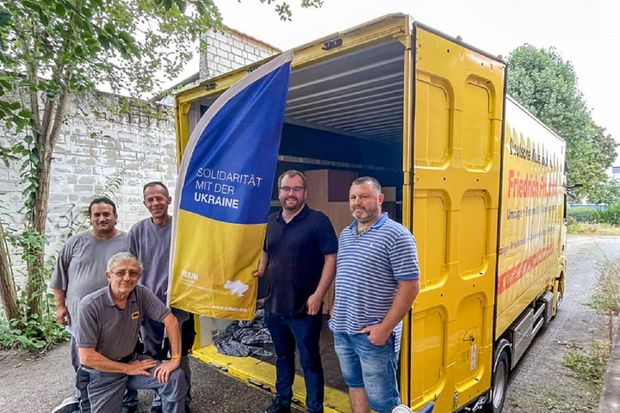 Team vor einem geöffneten Umzugsfahrzeug mit Fahne zur Solidarität mit der Ukraine.