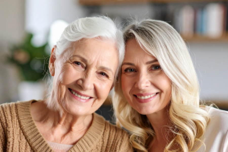 Ältere Frau und jüngere Frau sitzen eng beieinander und lächeln in einem gemütlichen Wohnumfeld