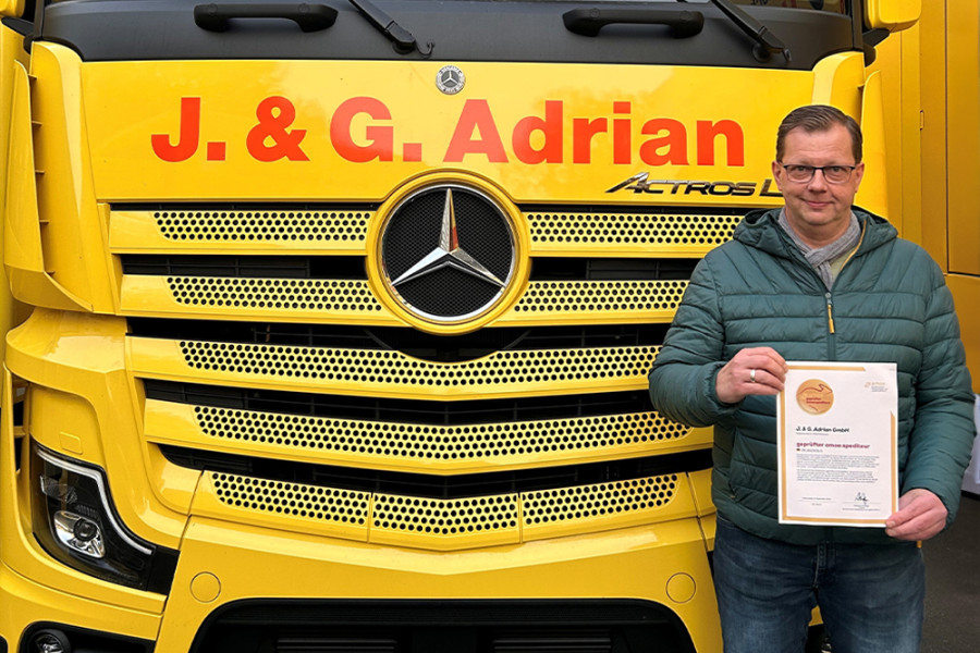 Mitarbeiter hält eine Auszeichnung vor einem gelben J. & G. Adrian Lkw