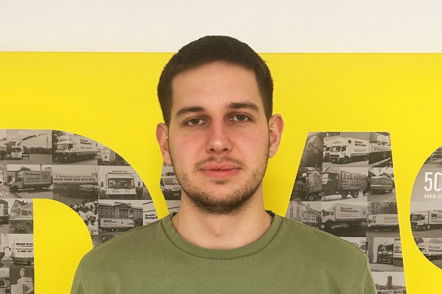 Mitarbeiterporträt vor gelber Wand mit historischen Fahrzeugmotiven