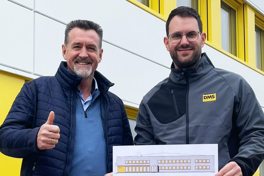 Zwei Personen stehen vor einem Firmengebäude und halten die Baupläne der neuen Fassadengestaltung von Friedrich Friedrich.