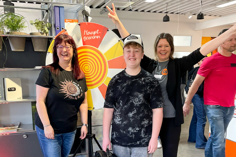 Gewinnspielteilnehmende stehen vor einem Glücksrad mit der Aufschrift ‚Hauptgewinn‘ bei einer Aktion im KS Büromöbel‑Showroom