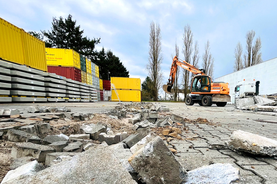 Bagger reißt beschädigte Pflastersteine bei Flächensanierung auf Industriegelände auf