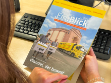 Eine Frau liest am Schreibtisch die Unternehmenszeitschrift „Ein.Blick“ (2025/02)